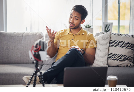 Content creator, laptop and phone, Indian man on sofa recording webinar, broadcast and live streaming in home. Internet, webcam and online influencer talking with equipment for social media channel. 118413676