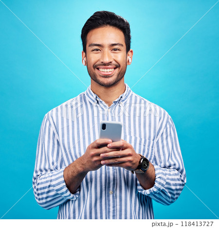 Happy, portrait and a man with a phone for communication isolated on a blue background in a studio. Smile, social media update and a person typing on a mobile for app, notification reply and message 118413727