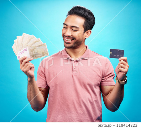 Credit card, smile and money by happy man in studio with savings, finance or investment growth on blue background. Cash, profit and asian guy excited for banking, loan or financial freedom isolated Credit card, smile and money by happy man in studio with savings, finance or investment growth on blue background. Cash, profit and asian guy excited for banking, loan or financial freedom isolated 118414222