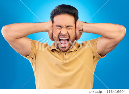 Man covering his ears while screaming in a studio for angry, upset or mad argument expression. Crazy, shout and young male person with an open mouth for loud voice gesture isolated by blue background 118416604