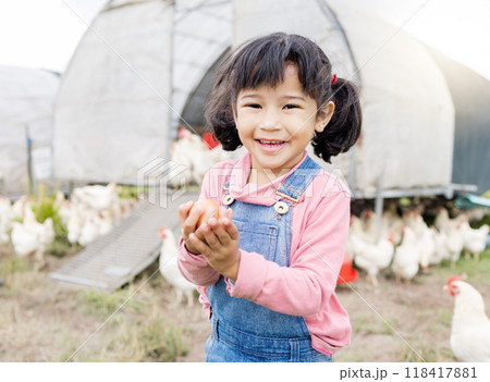 Portrait, Asian girl and farm for agriculture, chicken and happiness on holiday, vacation and holding eggs. Face, female child or kid in Japan, farming and sustainability with animals and countryside 118417881