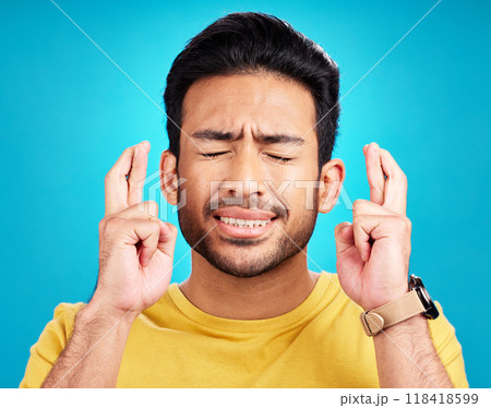 Luck, man and fingers crossed for hope in studio isolated on a blue background. Wish, hand gesture and male person with aspiration, hopeful emoji or wait for good fortune, results or optimistic faith 118418599