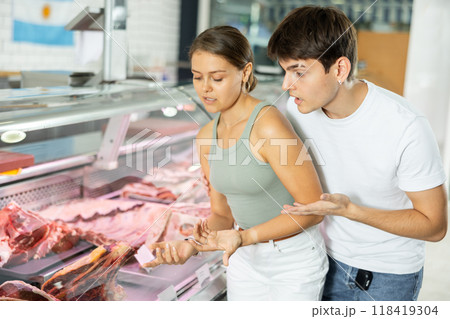 Spouse near butcher shop window inspects goods and choose piece of beef for cooking rib eye steak 118419304