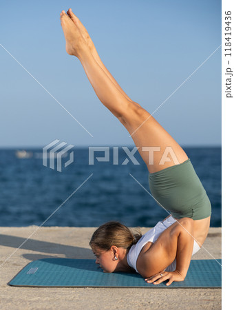 Sportive girl practicing chest stand pose of yoga on seashore 118419436