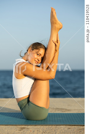 Sportive girl practicing boat pose of yoga on seashore Sportive girl practicing boat pose of yoga on seashore 118419528