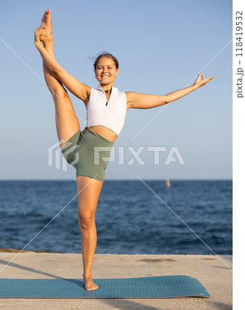 Sportive girl practicing extended hand to toe pose of yoga on seashore Sportive girl practicing extended hand to toe pose of yoga on seashore 118419532