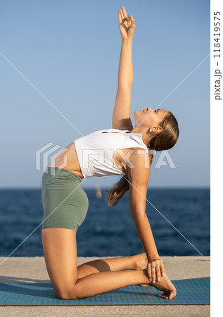 Athletic girl training camel position on mat on seashore 118419575
