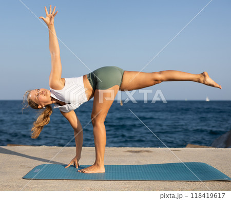 Athletic girl meditates in a yoga pose parshvottanasana on seashore 118419617
