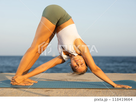 Sportive girl practicing revolved forward bend pose of yoga on seashore Sportive girl practicing revolved forward bend pose of yoga on seashore 118419664
