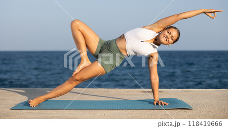 Positive girl practicing side plank pose of yoga on seashore Positive girl practicing side plank pose of yoga on seashore 118419666