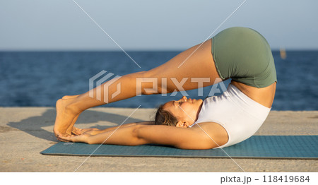 Sportive girl practicing shoulderstand pose of yoga on seashore Sportive girl practicing shoulderstand pose of yoga on seashore 118419684