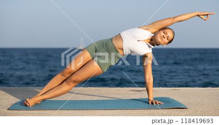 Positive girl practicing side plank pose of yoga on seashore 118419693