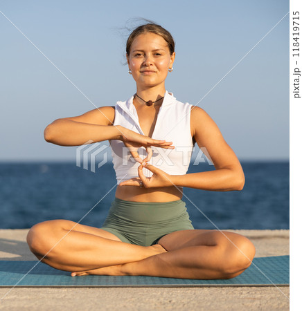 On windy day young slender woman does yoga near sea doing padmasana On windy day young slender woman does yoga near sea doing padmasana 118419715