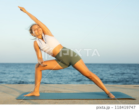 Sportive girl practicing triangle pose of yoga on seashore 118419747