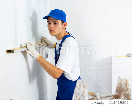 Builder checking quality of laid tiles on wall with level meter Builder checking quality of laid tiles on wall with level meter 118419863