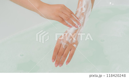 Two hands massage a creamy scrub onto the skin, creating a luxurious lather on the skin and under the water in the bathwater, creating a relaxing feeling suitable for advertising body care products Two hands massage a creamy scrub onto the skin, creating a luxurious lather on the skin and under the water in the bathwater, creating a relaxing feeling suitable for advertising body care products 118420248