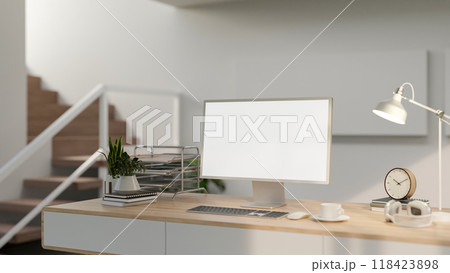 A minimalist home workspace features a computer with a white screen and objects on a wooden table. 118423898