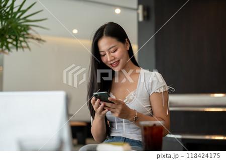 A beautiful, positive Asian woman using her smartphone while sitting in a modern coffee shop. A beautiful, positive Asian woman using her smartphone while sitting in a modern coffee shop. 118424175