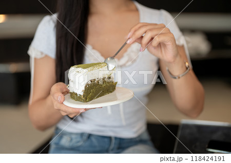 A close-up of a woman holding a plate of a matcha cake, eating a piece of cake in a coffee shop. A close-up of a woman holding a plate of a matcha cake, eating a piece of cake in a coffee shop. 118424191