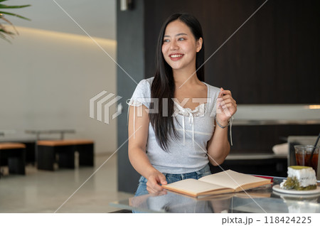 A woman sitting in a coffee shop, looking out the window for inspiration while writing in her book. A woman sitting in a coffee shop, looking out the window for inspiration while writing in her book. 118424225