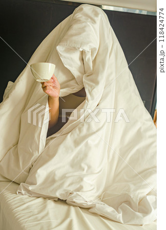 a person wrapped entirely in a blanket, resembling a ghost, holding a coffee cup. High quality photo 118424774