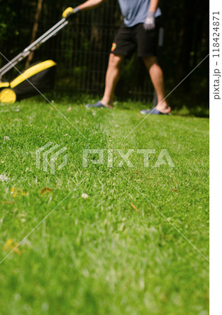 the gardener with a lawn mower is working in the backyard, a side view. High quality photo 118424871