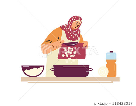 Muslim woman in a hijab standing at the table cutting ingredients into a saucepan. 118428017