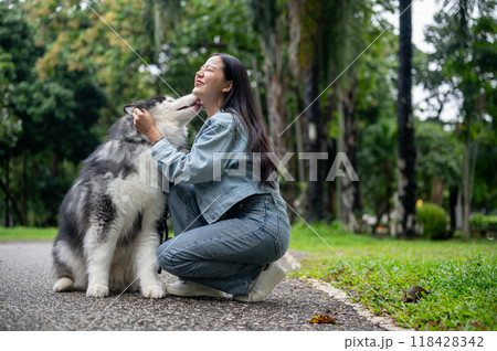 A cheerful Asian woman is sitting and playing with her Siberian husky in a green public park. A cheerful Asian woman is sitting and playing with her Siberian husky in a green public park. 118428342