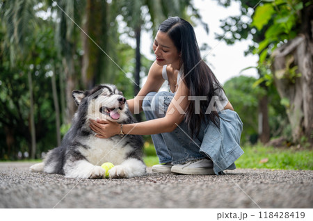 A cheerful Asian woman is playing with her dog in a park, giving him love and comfort. 118428419