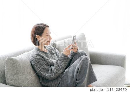 ソファーで寝転んでスマホをする女性 ソファーで寝転んでスマホをする女性 118428479