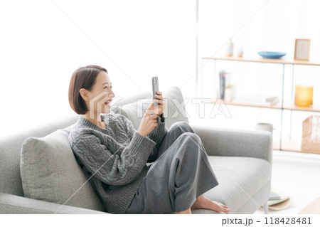 ソファーで寝転んでスマホをする女性 118428481