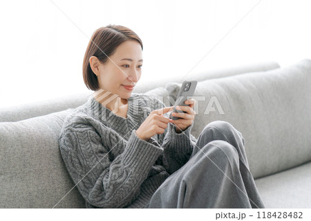 ソファーで寝転んでスマホをする女性 ソファーで寝転んでスマホをする女性 118428482