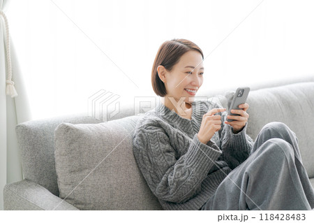 ソファーで寝転んでスマホをする女性 ソファーで寝転んでスマホをする女性 118428483