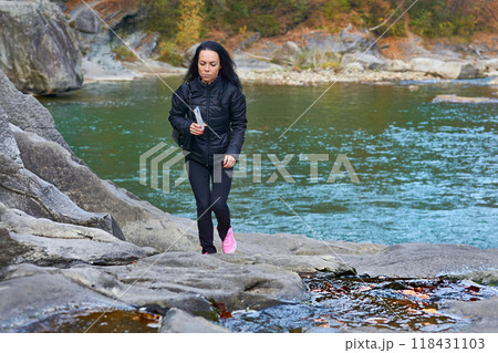 Young woman in black jacket walks along rocky bank of autumn mountain river Young woman in black jacket walks along rocky bank of autumn mountain river 118431103