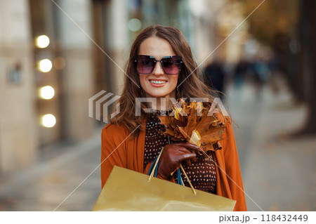 smiling trendy woman in orange trench coat with shopping bags 118432449