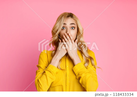 The image shows a young woman with long, blonde hair covering her mouth with her hands. She appears to be surprised or shocked. The background is a solid pink color. 118433334