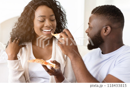 A couple enjoys a pizza together while sitting on a couch. A couple enjoys a pizza together while sitting on a couch. 118433815