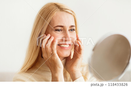 A woman with blonde hair looks into a mirror and smiles with a happy expression. 118433826
