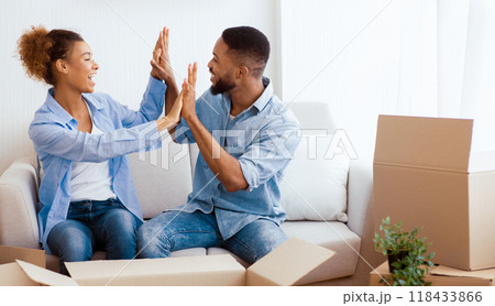 House Owners. Happy Afro Spouses Giving High-Five Sitting Among Unpacked Moving Boxes In Own Apartment. Copy Space 118433866