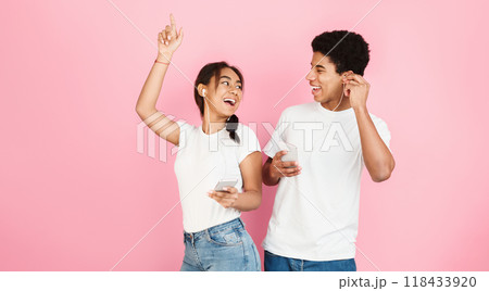 Happy students dancing and listening music by earphones over pink studio background Happy students dancing and listening music by earphones over pink studio background 118433920