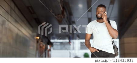 Successful african american guy talking on cellphone and smiling inside business center, panorama, copy space 118433935