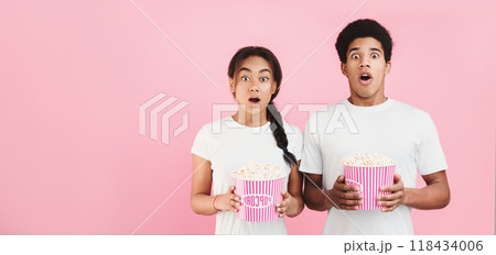 Scary movie. Shocked couple holding bucket of popcorn on pink background 118434006