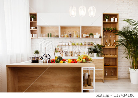 Modern kitchen island with fresh produce on display. The island is made of wood, has a white metal frame. There are several pieces of fruit and vegetables on the counter, including apples, oranges. Modern kitchen island with fresh produce on display. The island is made of wood, has a white metal frame. There are several pieces of fruit and vegetables on the counter, including apples, oranges. 118434100