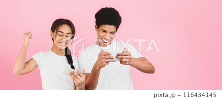 Happy couple playing together video games on mobile phones over pink background Happy couple playing together video games on mobile phones over pink background 118434145
