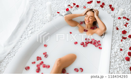 Body skin care. Woman enjoying milk bath with rose petals, relaxing in spa, free space 118434293