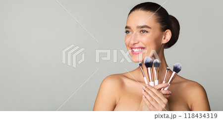 Excited Woman Holding Set of Makeup Brushes, Posing over Grey Background 118434319