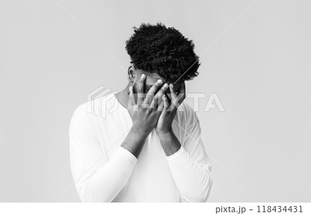 Young black man covering face with two hands, disappointed or stressed, orange studio background, copy space 118434431