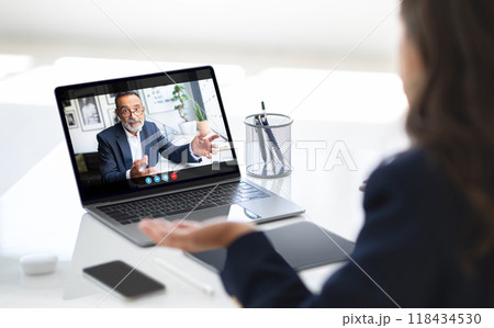 A businesswoman sits at her desk, engaged in a video call with a colleague on her laptop. She has a serious expression on her face, listening intently to the man on the screen A businesswoman sits at her desk, engaged in a video call with a colleague on her laptop. She has a serious expression on her face, listening intently to the man on the screen 118434530
