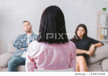 A woman sits in a chair, facing away from the camera, listening intently as a couple sits on a couch behind her. The woman, likely a therapist, appears to be focused on the couple A woman sits in a chair, facing away from the camera, listening intently as a couple sits on a couch behind her. The woman, likely a therapist, appears to be focused on the couple 118434560