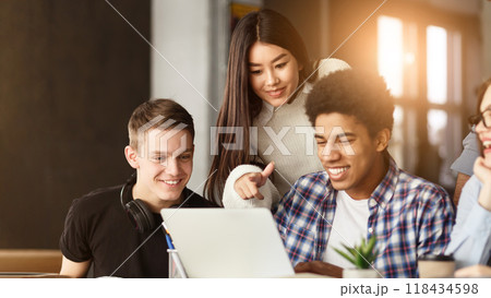 A diverse group of students are gathered around a laptop, attentively looking at the screen. They appear to be engaged in a discussion or viewing content together. 118434598